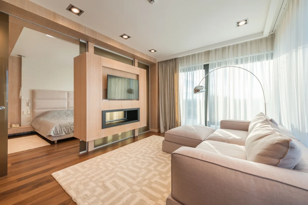 Modern studio apartment layout featuring a space-saving wooden room divider with a built-in TV mount and fireplace separating the living area and bedroom.